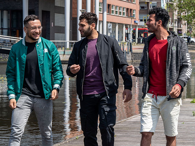 Three male students walking along river chatting